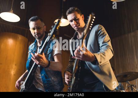medium shot di due giovani chitarristi che suonano in uno studio con la loro band, musica concept. Foto di alta qualità Foto Stock
