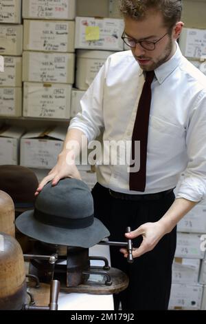 Il membro dello staff di Lock & Co Hatters usa Steam per rimodellare un cappello, Londra, Regno Unito. Foto Stock