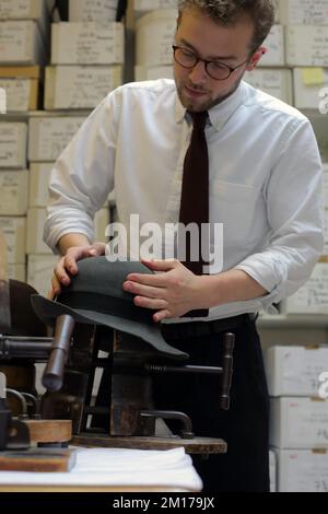 Il membro dello staff di Lock & Co Hatters usa Steam per rimodellare un cappello, Londra, Regno Unito. Foto Stock