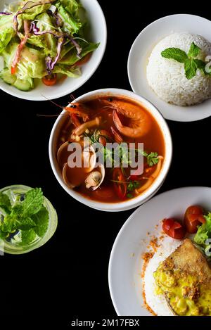 Pranzo a base di zuppa di tom yum, insalata, pesce basco alla griglia, riso, limonata su sfondo nero Foto Stock