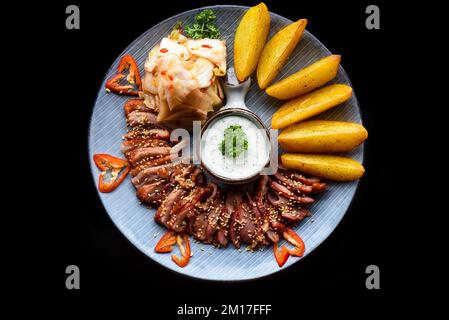 Filetto d'oca fritto con aglio servito con spicchi di patate e kim chi su sfondo nero vista dall'alto Foto Stock