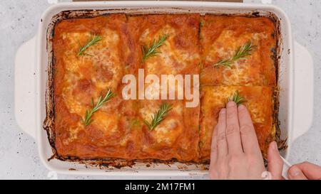 Lasagne di spinaci appena sfornate in forno da vicino sul tavolo da cucina. Donna taglia lasagne a fette. Foto Stock