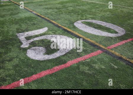 50 yard line su un campo americano di calcio di scuola superiore con numeri bianchi e erba sintetica verde, insieme a linee aggiuntive. Foto Stock