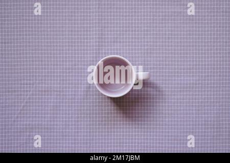 Tazza vuota sullo sfondo del tessuto viola a motivo di controllo. vista dall'alto Foto Stock