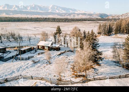 Paesaggio rurale, villaggio siberiano, Russia, bellissimo paesaggio rurale in inverno. Casa in legno villaggio sullo sfondo delle montagne. Foto Stock