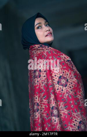 Bella donna in hijab nero con batik da Jambi, Indonesia. Foto Stock