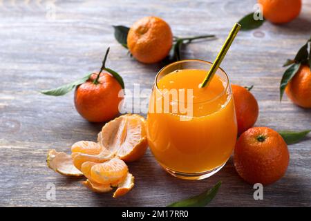 Succo di mandarino appena spremuto con mandarini freschi sul tavolo di legno grigio, fuoco selettivo, spazio Foto Stock