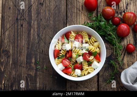 Insalata fatta in casa con pasta, pomodori, feta e spezie su tavola di legno. cibo semplice e delizioso. vista dall'alto, spazio Foto Stock