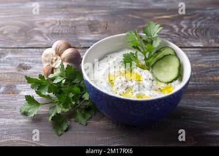 Tradizionale salsa tzatziki allo yogurt greco con cetrioli ed erbe su sfondo di legno Foto Stock