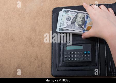 Mano che tiene le banconote del dollaro americano sulla calcolatrice Foto Stock