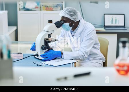 Vista laterale ritratto di scienziato nero utilizzando il microscopio in laboratorio medico, spazio copia Foto Stock