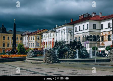 Banska Bystrica, Slovacchia - 15 agosto 2021: Vista di Piazza SNP - edifici storici colorati, fontana e monumento, nubi tempestose grigie. Foto Stock