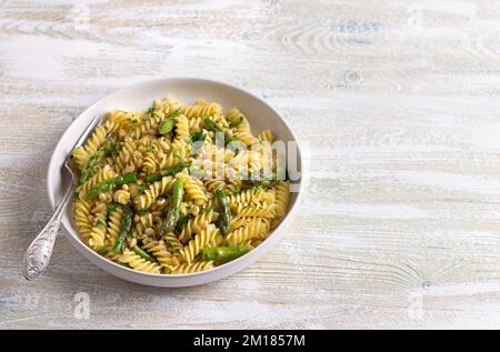 Pasta vegana con asparagi, aglio, pinoli e prezzemolo su sfondo ligneo. Semplice cibo fatto in casa Foto Stock