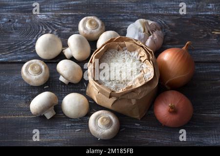 Ingredienti per un delizioso piatto vegano. Riso basmati bianco, aglio e champignons su un tavolo di legno, vista dall'alto, orizzontale Foto Stock