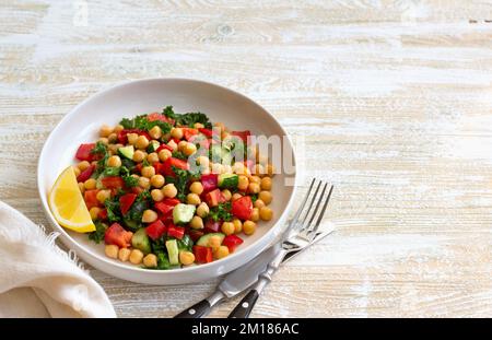 Insalata vegana sana con ceci, pomodori, cetrioli, peperoni e kale su sfondo di legno chiaro, spazio Foto Stock