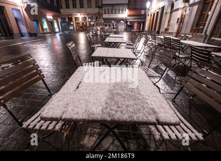 11 dicembre 2022, Hessen, Francoforte sul meno: Un sottile strato di neve appena caduta si trova sui tavoli di fronte a un bar nella nuova città vecchia di Francoforte sul meno durante l'alba. Foto: Frank Rumpenhorst/dpa Foto Stock