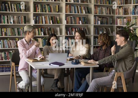 Allegro team di studenti universitari multietnici che studiano in biblioteca pubblica Foto Stock