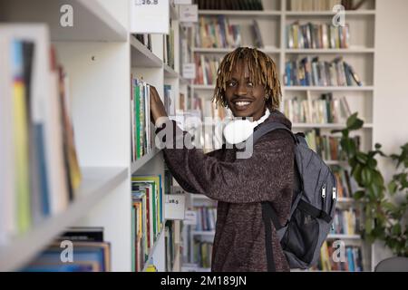 Allegro soddisfatto ragazzo studente nero scegliendo libro di testo sullo scaffale Foto Stock