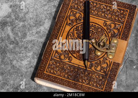 Giornale in pelle, goffrato con il design Celtic Tree of Life, con carta riciclata e penna stilografica. Su uno sfondo di pietra scura Foto Stock