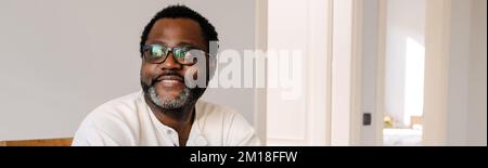Felice uomo afroamericano maturo che indossa occhiali sorridenti mentre riposa a casa Foto Stock
