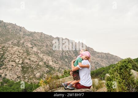 Bambino con cancro che abbraccia sua madre in natura. Indossa una sciarpa rosa sulla testa Foto Stock