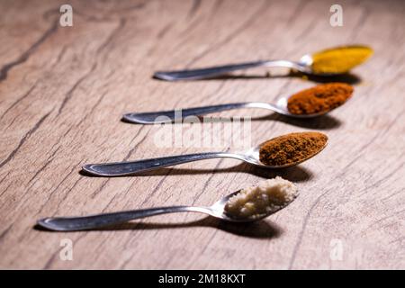 Spezie tipiche brasiliane - mandorle, cannella, paprika e curcuma in polvere in un cucchiaio su un tavolo di legno rustico. Foto Stock