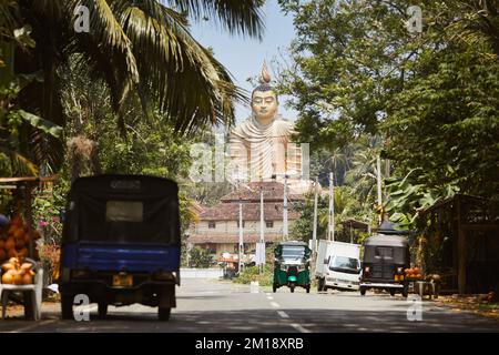 Traffico su strada rurale contro la statua di Buddha. Wewurukannala Buduraja Maha Viharaya tempio buddista a Dikwella, Sri Lanka. Foto Stock