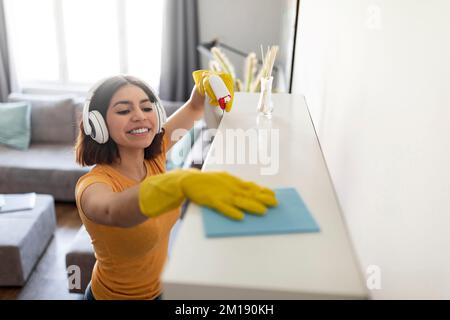 Faccende domestiche. Giovane donna araba pulente polvere da scaffale a casa Foto Stock