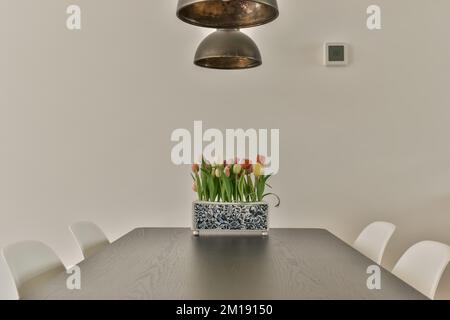 una sala da pranzo con sedie bianche e un tavolo di legno davanti ad una grande lampada a sospensione appesa sopra il tavolo Foto Stock