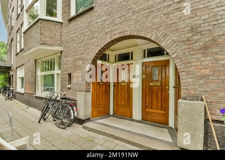 un edificio in mattoni con due biciclette parcheggiate nelle porte e una bici appoggiata al muro dall'altro lato Foto Stock