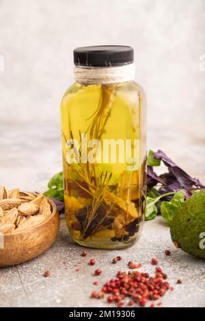 Olio di girasole in vaso di vetro con varie erbe e spezie, sesamo, rosmarino, avocado, basilico, mandorla su fondo di cemento marrone. Vista laterale, selezionare Foto Stock