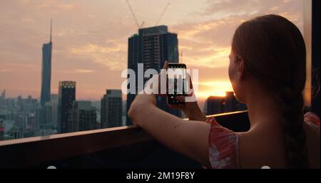 Donna turistica che fotografa i grattacieli del paesaggio urbano al tramonto nella capitale della Malesia. Nuvoloso crepuscolo vista skyline pesca dal tetto di un apar Foto Stock