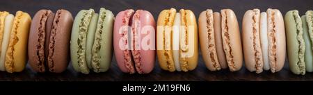 dolci e colorati macaron francesi allineati su tavola di legno scuro, dessert. panorama Foto Stock