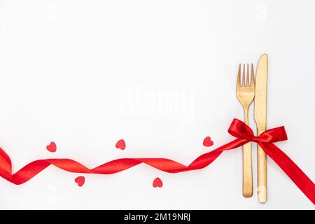 Coltello e forchetta legati con un nastro rosso in una banca su sfondo bianco. Foto Stock