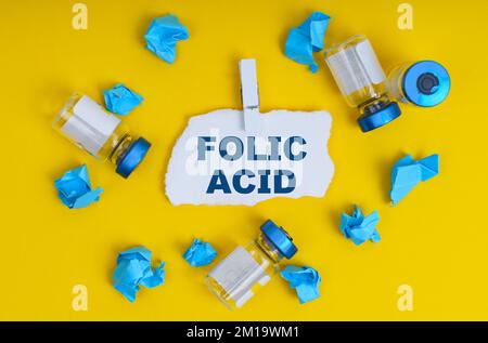 Medicina e concetto di salute. Su fondo giallo ci sono ampolle, carta stropicciata blu e carta con l'iscrizione - ACIDO FOLICO Foto Stock