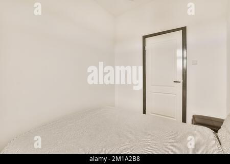 una camera da letto con pareti bianche e rifiniture nere intorno al letto, c'è una porta che conduce ad un'altra stanza Foto Stock