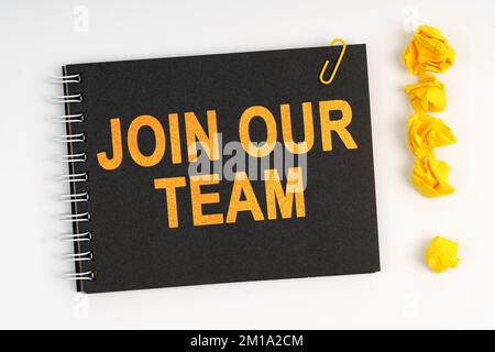 Concetto aziendale. Su uno sfondo bianco si trova un marcatore, un punto esclamativo fatto di carta e un notebook con l'iscrizione - UNISCITI AL NOSTRO TEAM Foto Stock
