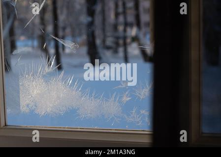 ghiaccio congelato su un vetro della finestra in una fredda giornata invernale. la luce del sole splende attraverso il vetro della stanza, creando le ombre di fiori di ghiaccio sul legno Foto Stock