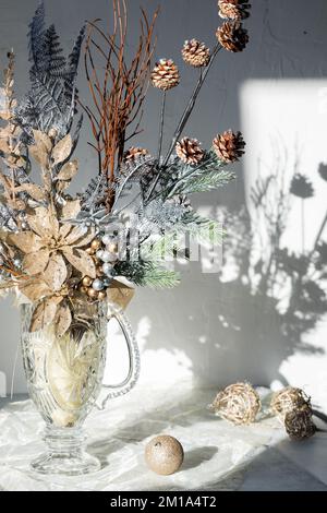 Bouquet natalizio invernale in un vaso di cristallo d'epoca con luce del sole in streaming. Foto Stock