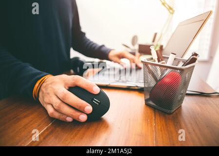 L'uomo che utilizza un mouse ottico verticale nero per computer dal design ergonomico e lascia il normale mouse per computer nel cestino. Foto Stock