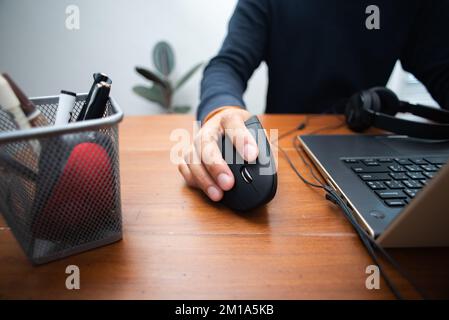 L'uomo che utilizza un mouse ottico verticale nero per computer dal design ergonomico e lascia il normale mouse per computer nel cestino. Foto Stock