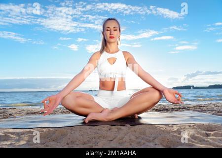 Giovane donna attraente che pratica yoga sulla riva del lago. Foto Stock
