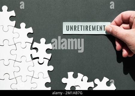 Immagine del concetto di non pensionamento. Pezzi di puzzle a metà assemblati e separati. Mano che tiene pezzo di carta, nota appiccicosa con la parola Unretention su di esso. Vista dall'alto Foto Stock