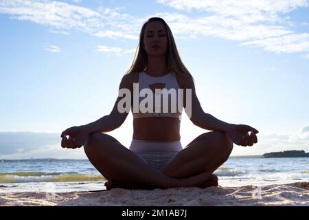 attraente donna che pratica yoga vicino al lago. foto nella luce di sfondo. Silhouette in posizione lotus. Foto Stock