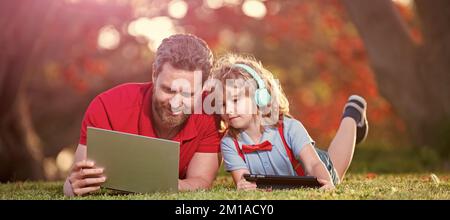 Banner di padre su figlio ragazzo scuola con notebook studio online giacente su erba, formazione online su laptop. padre e figlio usano la comunicazione moderna Foto Stock