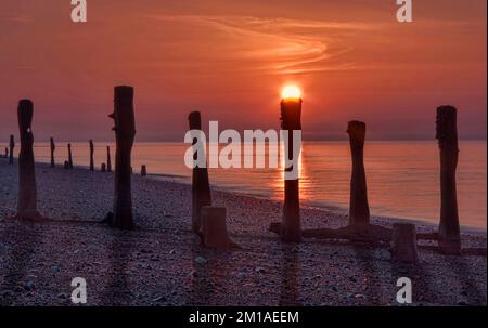 Sole che sorge sopra un vecchio Groyne di legno su una spiaggia con bassa marea Foto Stock