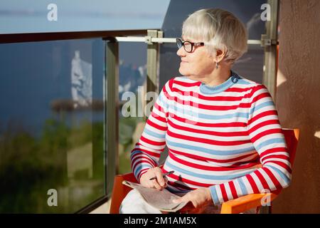 Donna anziana in bicchieri seduti sul balcone vicino al mare Foto Stock