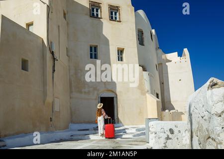 Una giovane donna con una valigia rossa cammina per le vecchie strade della Grecia Foto Stock