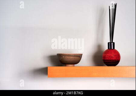 diffusore a lamelle e piccola ciotola su ripiano di legno con ombre sulla parete Foto Stock