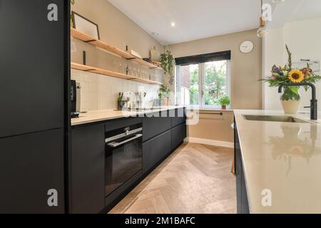 una cucina moderna con armadietti neri e countertops bianchi al centro dell'immagine è una finestra aperta che si affaccia sul Foto Stock